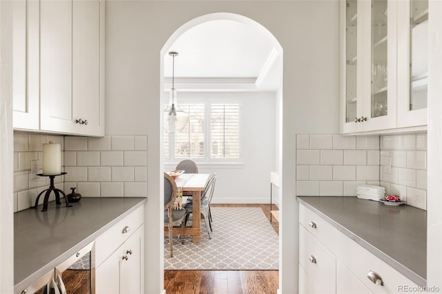 kitchen with dark wood-type flooring, backsplash, white cabinetry, arched walkways, and glass insert cabinets