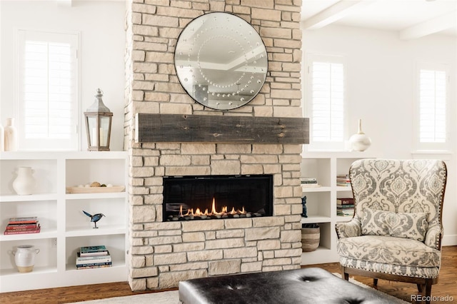 living room with beam ceiling, a healthy amount of sunlight, a large fireplace, and wood finished floors