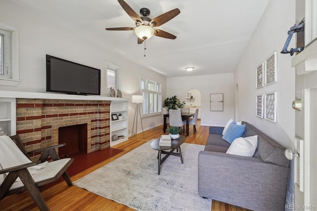 living room featuring wood finished floors, a fireplace, a ceiling fan, and baseboards