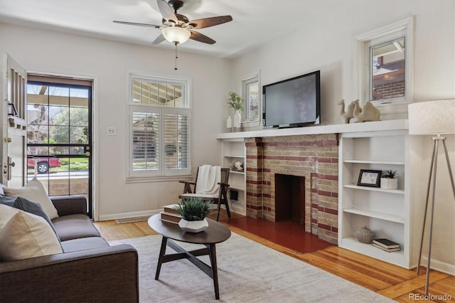 living room featuring wood finished floors, a ceiling fan, a fireplace, and baseboards