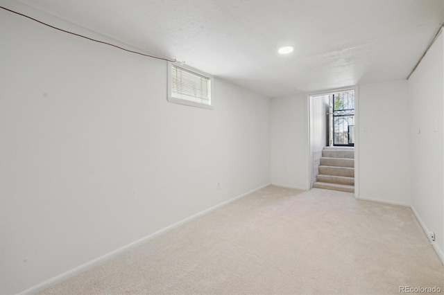 below grade area featuring light colored carpet, baseboards, and stairway