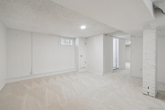 below grade area featuring light colored carpet, baseboards, and a textured ceiling