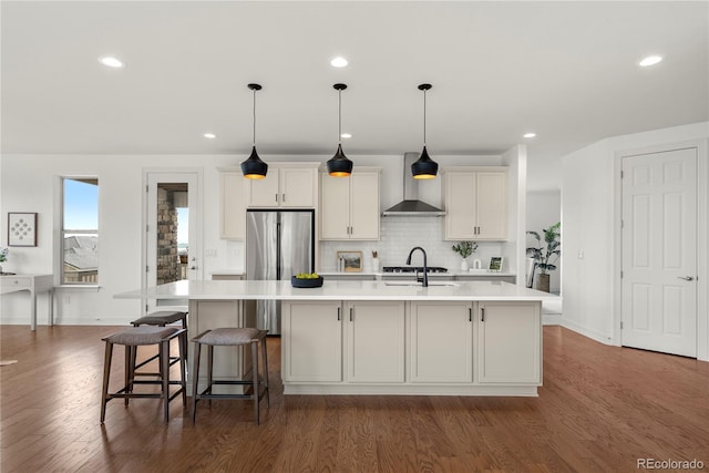 9566 Poppy Way, Arvada, CO 80007 - kitchen featuring wall chimney range hood, stainless steel refrigerator, light countertops, a spacious island, and dark wood-style floors