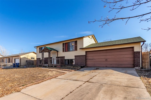 split foyer home featuring brick siding, an attached garage, driveway, and fence