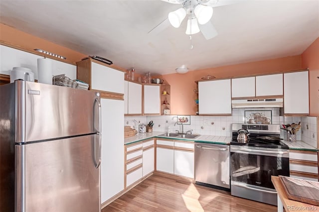 kitchen with under cabinet range hood, white cabinets, appliances with stainless steel finishes, and a sink