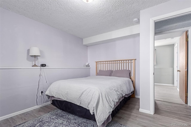 bedroom featuring a textured ceiling, baseboards, and wood finished floors