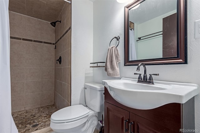 full bathroom with vanity, toilet, a textured wall, and a tile shower