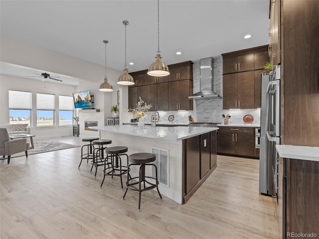 kitchen with a kitchen island with sink, dark brown cabinets, wall chimney exhaust hood, and hanging light fixtures