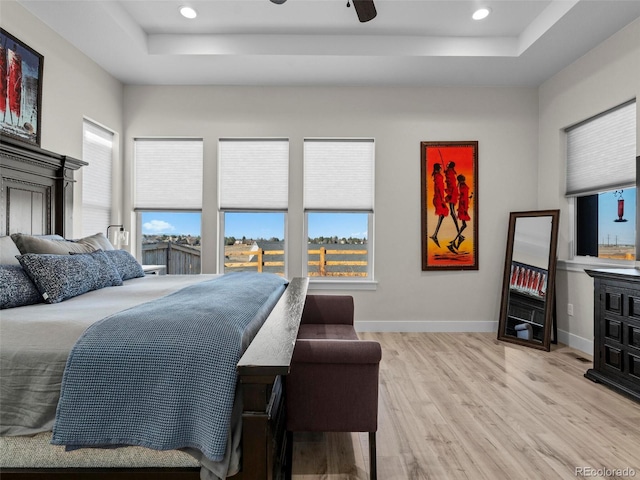 bedroom with a raised ceiling, ceiling fan, and light hardwood / wood-style floors