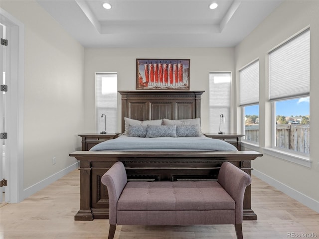 bedroom featuring a raised ceiling, multiple windows, and light hardwood / wood-style floors