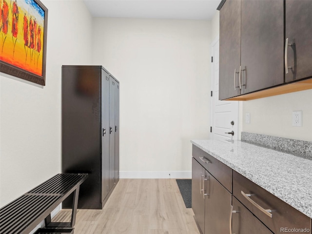 kitchen with light stone countertops, dark brown cabinets, and light wood-type flooring