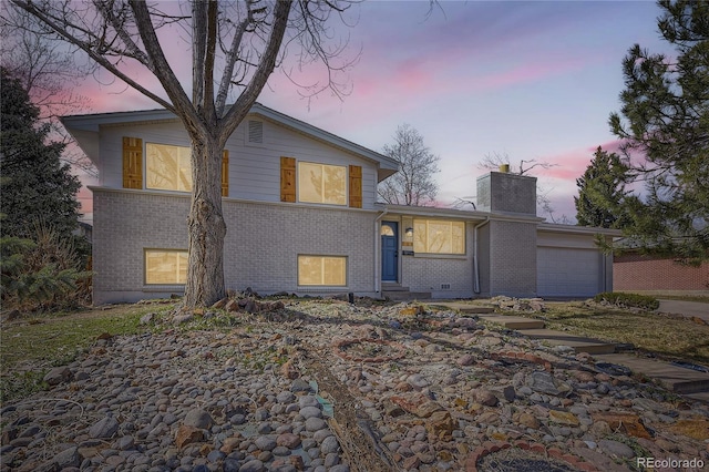 tri-level home with brick siding, a chimney, and a garage