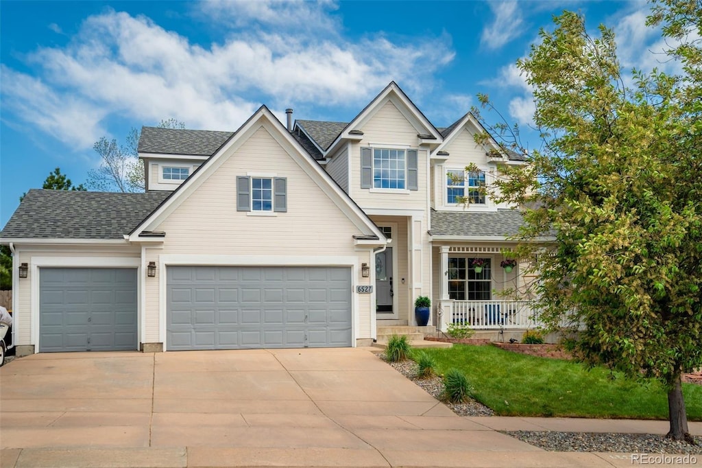 view of front of home with covered porch, driveway, a shingled roof, an attached garage, and a front yard