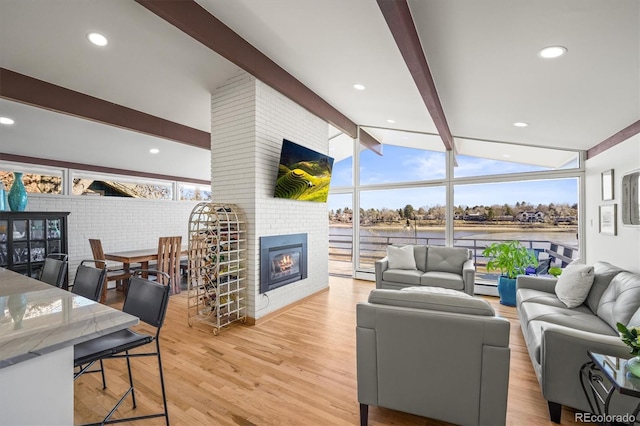 living area with a baseboard heating unit, lofted ceiling with beams, recessed lighting, light wood-style flooring, and a fireplace