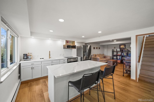 kitchen with a breakfast bar, light wood-style flooring, a sink, a baseboard heating unit, and stainless steel appliances