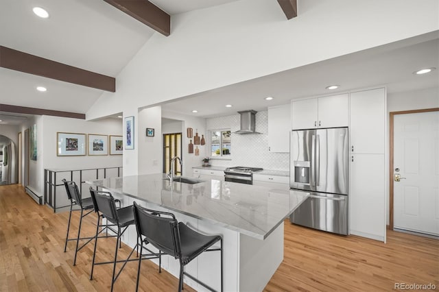 kitchen featuring wall chimney range hood, a sink, appliances with stainless steel finishes, a baseboard heating unit, and a kitchen breakfast bar