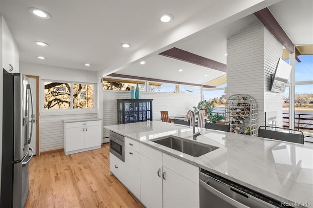 kitchen with light stone counters, a sink, stainless steel appliances, white cabinets, and light wood-style floors