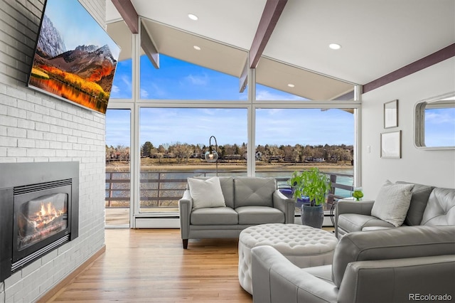 living area with a wealth of natural light, a fireplace, a wall of windows, and wood finished floors