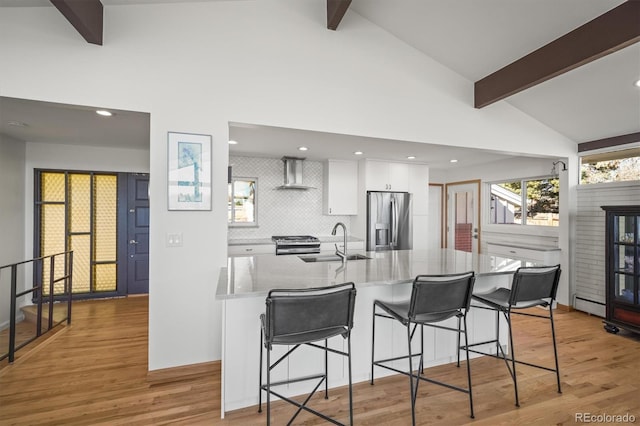 kitchen with a sink, appliances with stainless steel finishes, white cabinetry, wall chimney exhaust hood, and light wood-type flooring