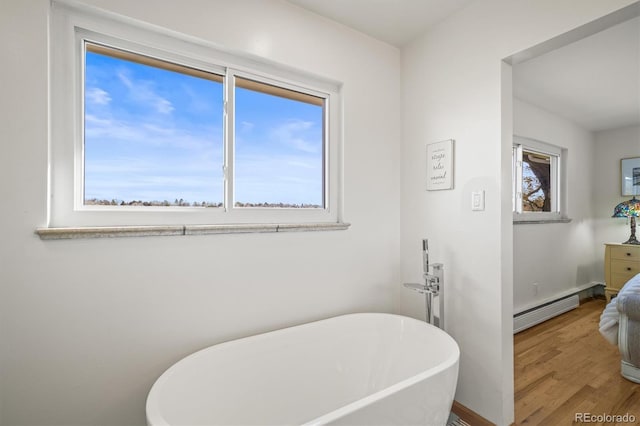 full bath featuring baseboards, baseboard heating, wood finished floors, and a freestanding bath