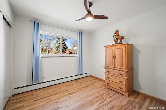 unfurnished bedroom with a baseboard heating unit, a closet, light wood finished floors, baseboards, and ceiling fan