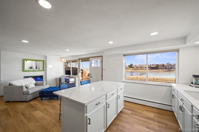 kitchen featuring light stone counters, a baseboard heating unit, open floor plan, and light wood-style flooring