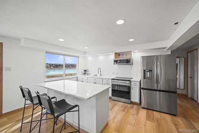 kitchen featuring a breakfast bar, light wood-style flooring, a sink, appliances with stainless steel finishes, and light countertops