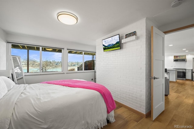 bedroom with multiple windows, light wood-type flooring, and brick wall