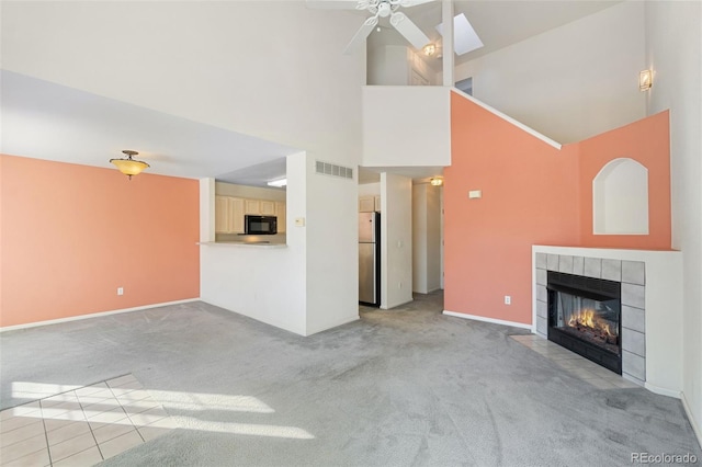 unfurnished living room featuring a tiled fireplace, ceiling fan, light carpet, and high vaulted ceiling