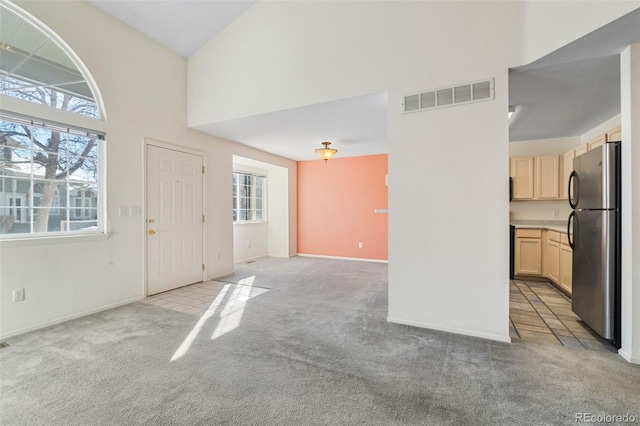 unfurnished living room with lofted ceiling, a healthy amount of sunlight, and light carpet