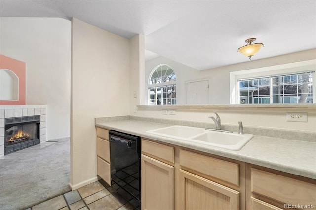 kitchen featuring black dishwasher, sink, a tiled fireplace, light colored carpet, and light brown cabinets