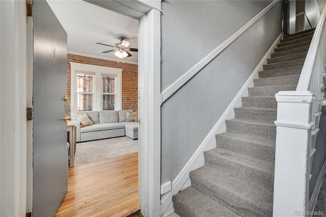 stairway featuring hardwood / wood-style floors, ceiling fan, ornamental molding, and brick wall