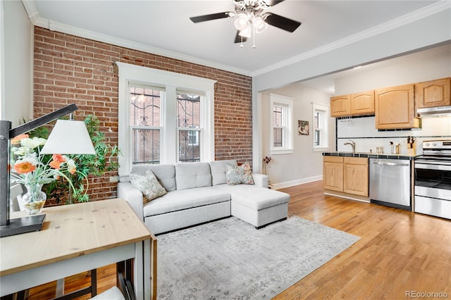 living room with ceiling fan, sink, brick wall, crown molding, and light hardwood / wood-style floors