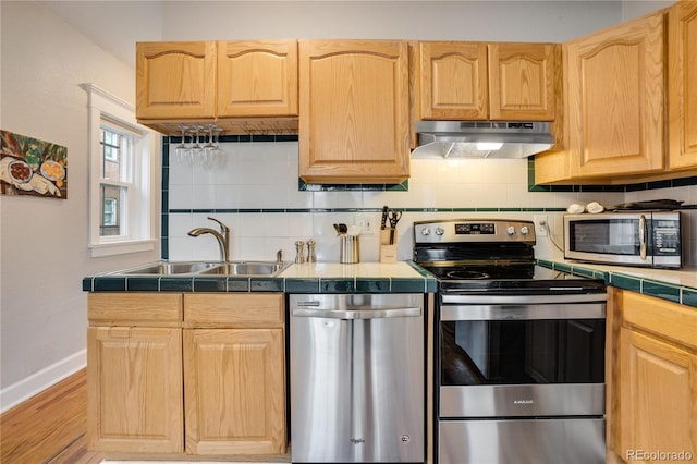 kitchen featuring sink, light brown cabinets, backsplash, tile countertops, and appliances with stainless steel finishes