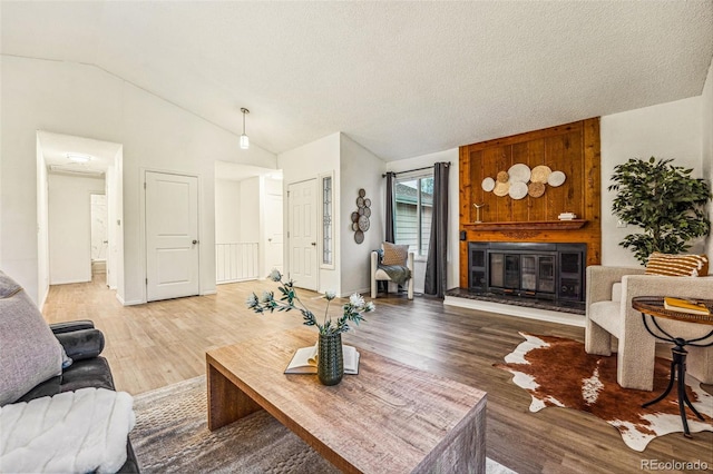 living area with a fireplace, vaulted ceiling, a textured ceiling, and light wood finished floors