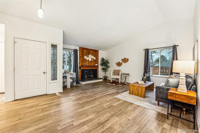 living room with a large fireplace, a healthy amount of sunlight, vaulted ceiling, and light wood finished floors