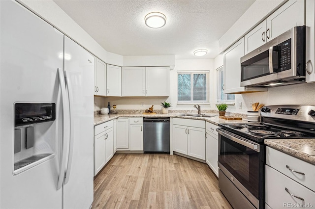 kitchen with white cabinets, light wood-style flooring, stainless steel appliances, and a sink