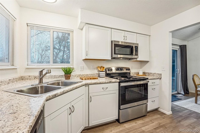 kitchen featuring stainless steel appliances, a sink, white cabinets, light countertops, and light wood finished floors