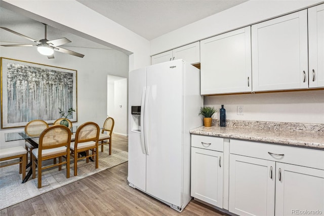 kitchen featuring white fridge with ice dispenser, a ceiling fan, light wood-style flooring, and white cabinets