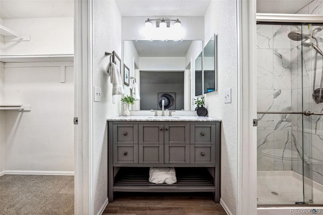 bathroom featuring a marble finish shower, baseboards, a textured wall, wood finished floors, and vanity