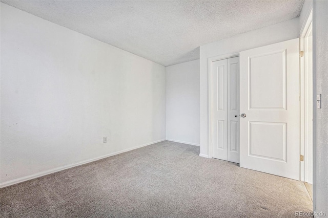 unfurnished bedroom with carpet floors, a closet, a textured ceiling, and baseboards