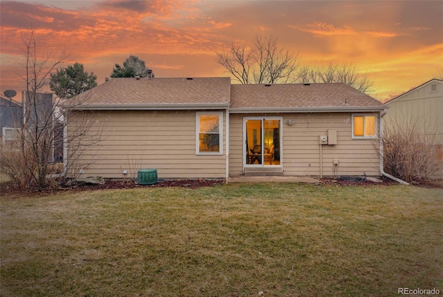 rear view of property featuring a shingled roof, a lawn, and a patio