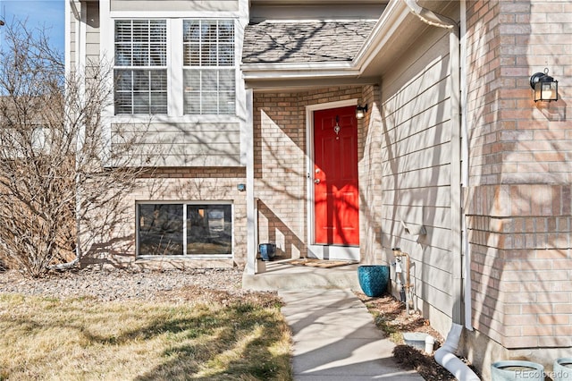 doorway to property featuring brick siding and roof with shingles