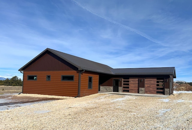 view of front facade featuring an exterior structure, an attached garage, metal roof, faux log siding, and an outdoor structure