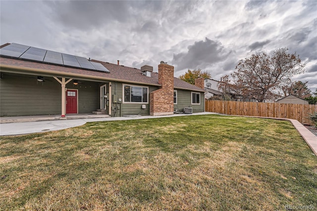 rear view of house featuring central AC unit, a lawn, solar panels, and a patio