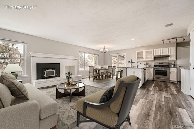 living room featuring a brick fireplace, a notable chandelier, a textured ceiling, hardwood / wood-style flooring, and sink