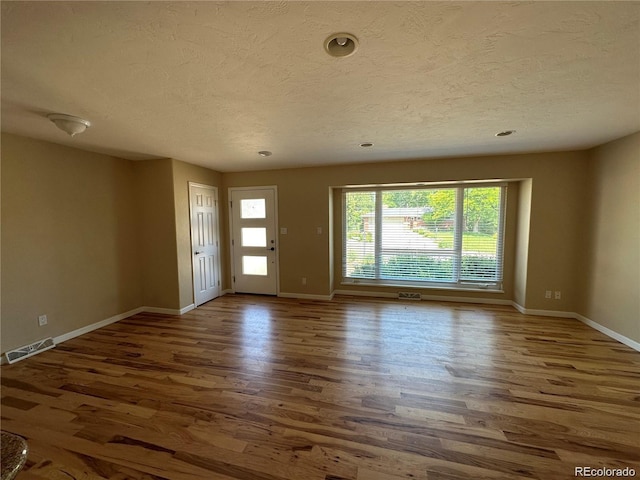 interior space with a textured ceiling, visible vents, wood finished floors, and baseboards