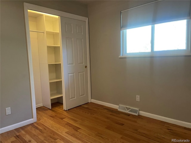unfurnished bedroom featuring baseboards, a closet, visible vents, and wood finished floors