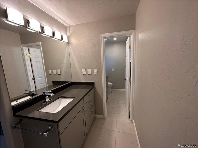 bathroom with toilet, baseboards, tile patterned flooring, a textured wall, and vanity