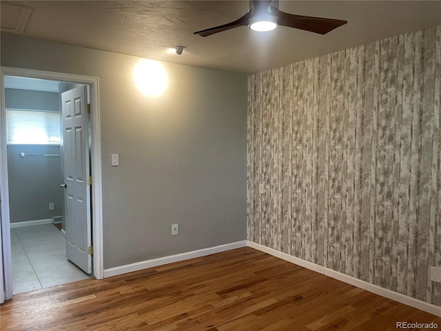 spare room with attic access, baseboards, a ceiling fan, and wood finished floors